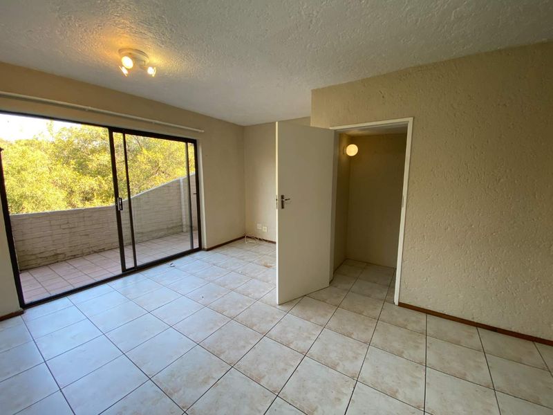 An empty bedroom featuring tiled flooring, a built-in cupboard, and a sliding glass door providing access to an outdoor balcony area.