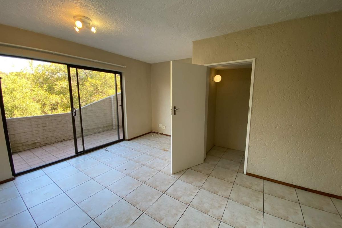 An empty bedroom featuring tiled flooring, a built-in cupboard, and a sliding glass door providing access to an outdoor balcony area.
