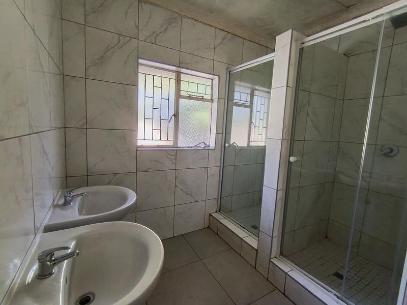 A functional bathroom featuring a double vanity, a glass-enclosed shower, and tiled finishes, currently awaiting ceiling completion.