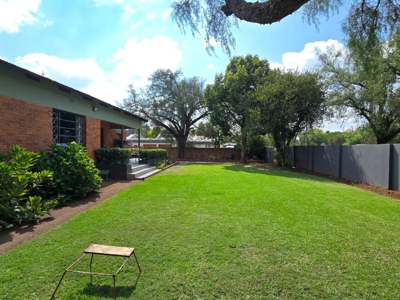 A spacious rear garden featuring a well-maintained lawn, brick exterior facade, and a secure boundary wall.