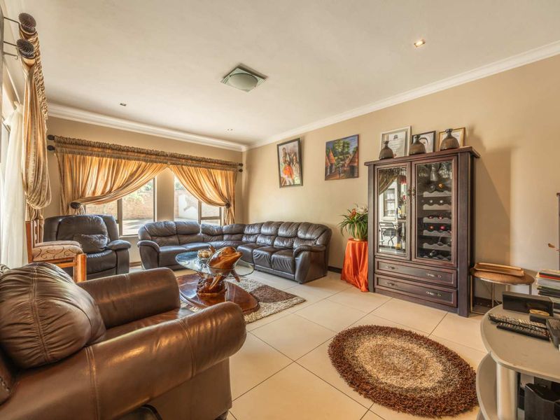 A spacious living room featuring neutral tiled flooring, recessed downlighting, and large windows with decorative curtains, creating a comfortable and well-lit living space.