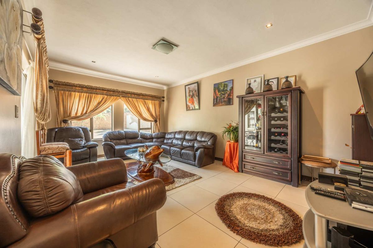 A spacious living room featuring neutral tiled flooring, recessed downlighting, and large windows with decorative curtains, creating a comfortable and well-lit living space.