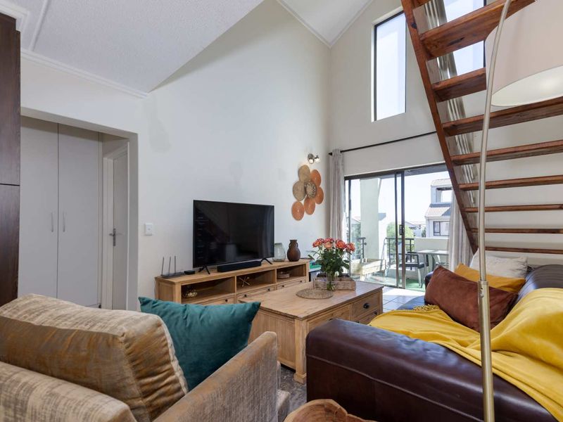 Spacious living room featuring a vaulted ceiling, wooden staircase, and large windows providing natural light and access to the balcony.