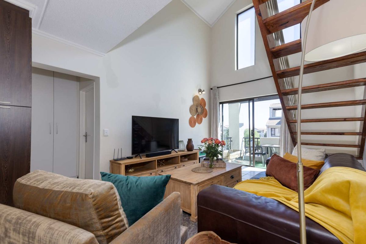 Spacious living room featuring a vaulted ceiling, wooden staircase, and large windows providing natural light and access to the balcony.