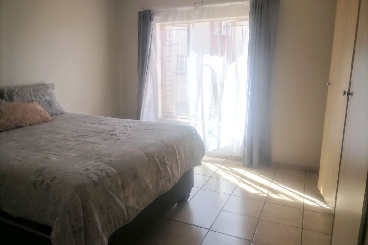 A bedroom featuring tiled flooring and a built-in wardrobe, with natural light streaming through a window fitted with security bars.