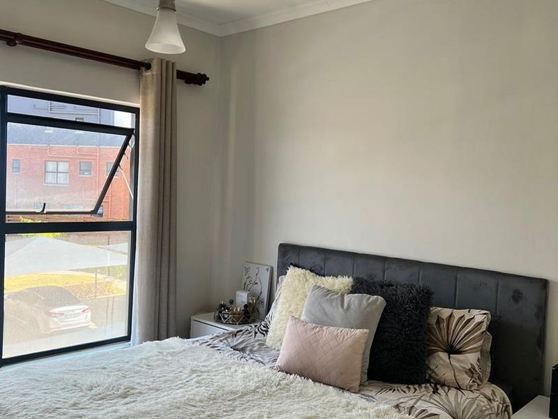 A well-lit bedroom featuring a large casement window, neutral wall finishes, and a central pendant light fixture.