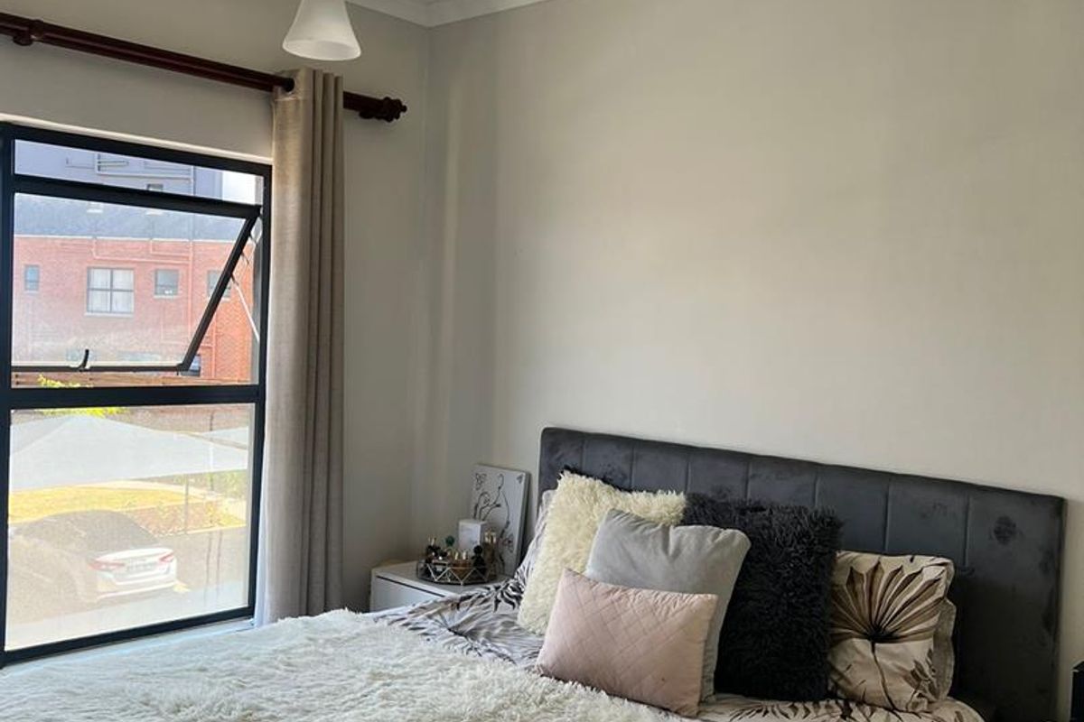 A well-lit bedroom featuring a large casement window, neutral wall finishes, and a central pendant light fixture.