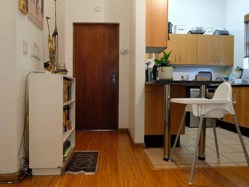 A functional kitchen area featuring wooden cabinetry, laminate countertops, and a breakfast bar, transitioning from laminate flooring to tiled kitchen flooring.