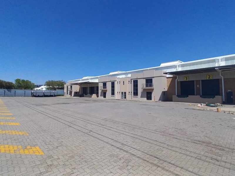 Industrial warehouse facility featuring multiple loading docks with roller shutter doors and a large paved yard area for logistics and vehicle access.