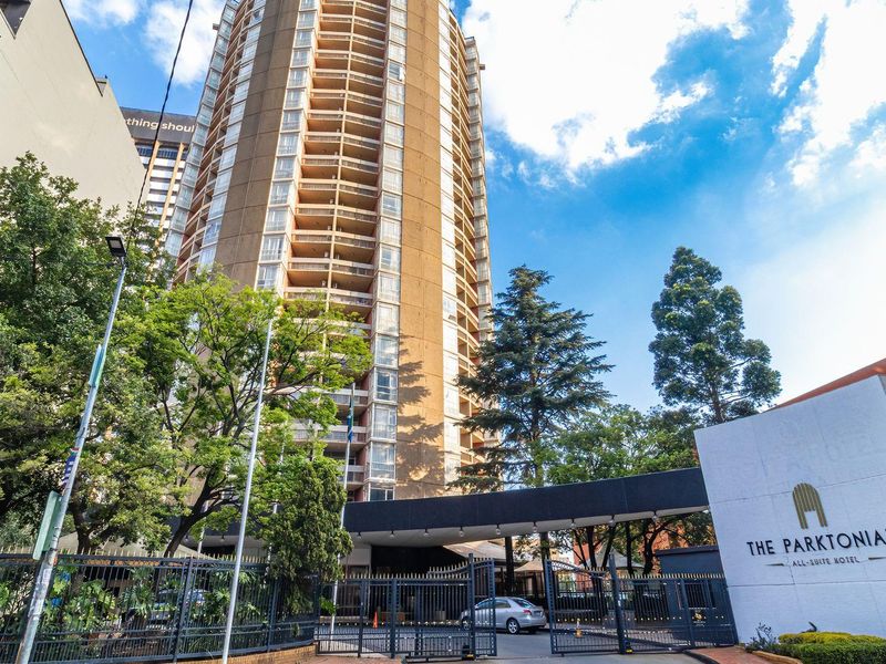 Exterior view of The Parktonian high-rise apartment building, featuring a secure gated entrance, driveway, and prominent building signage.