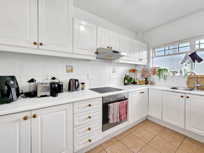 A well-maintained kitchen featuring white cabinetry, tiled backsplash, built-in oven with electric cooktop, and a stainless steel sink.