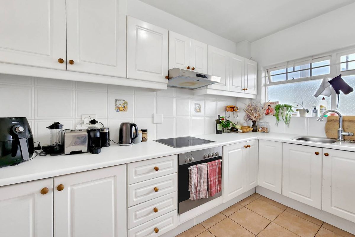 A well-maintained kitchen featuring white cabinetry, tiled backsplash, built-in oven with electric cooktop, and a stainless steel sink.