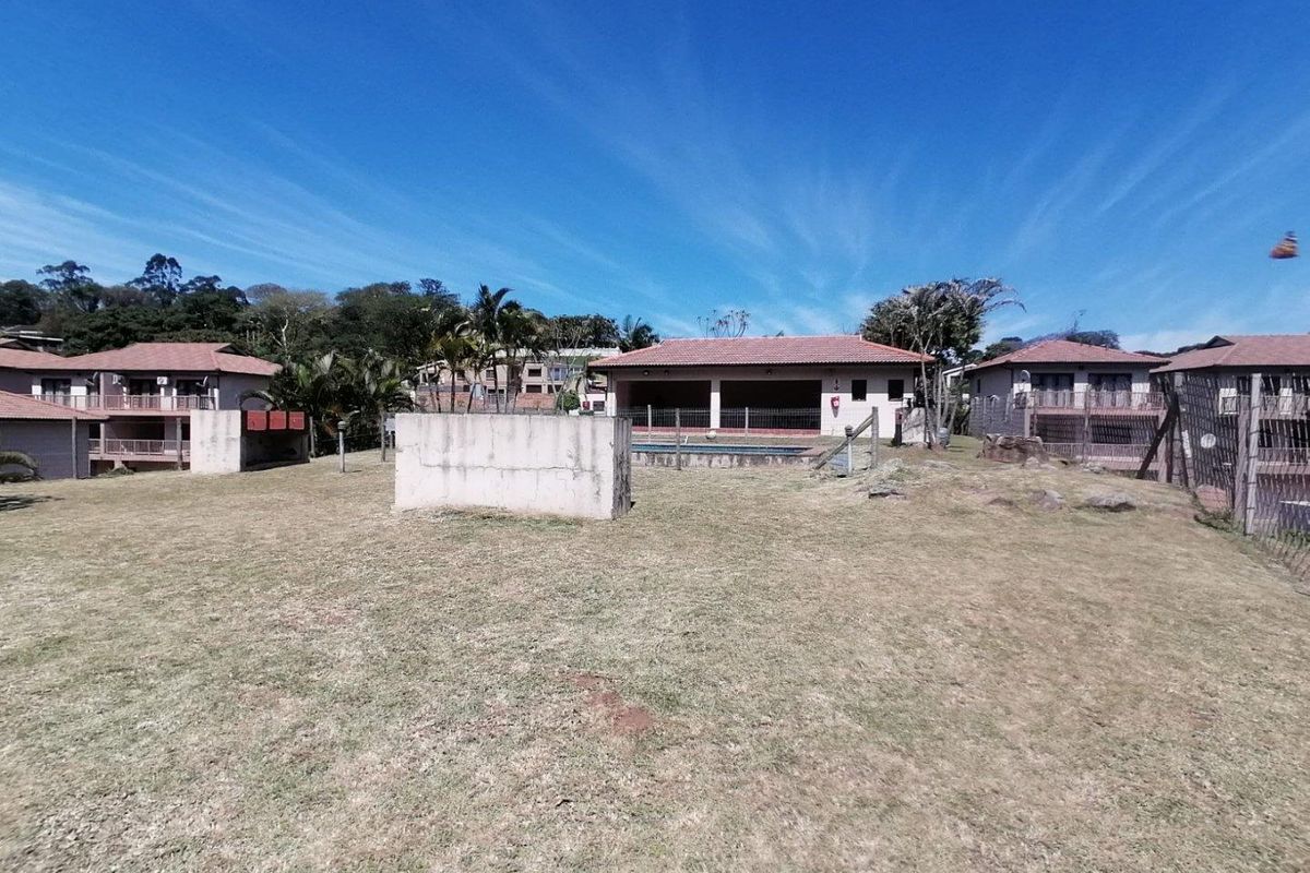 Rear view of the townhouse featuring a covered patio, swimming pool, and a large open lawn area within a residential complex.