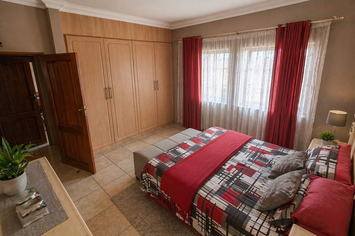 A well-maintained bedroom featuring built-in wooden cupboards, tiled flooring, and large windows with curtain rails.