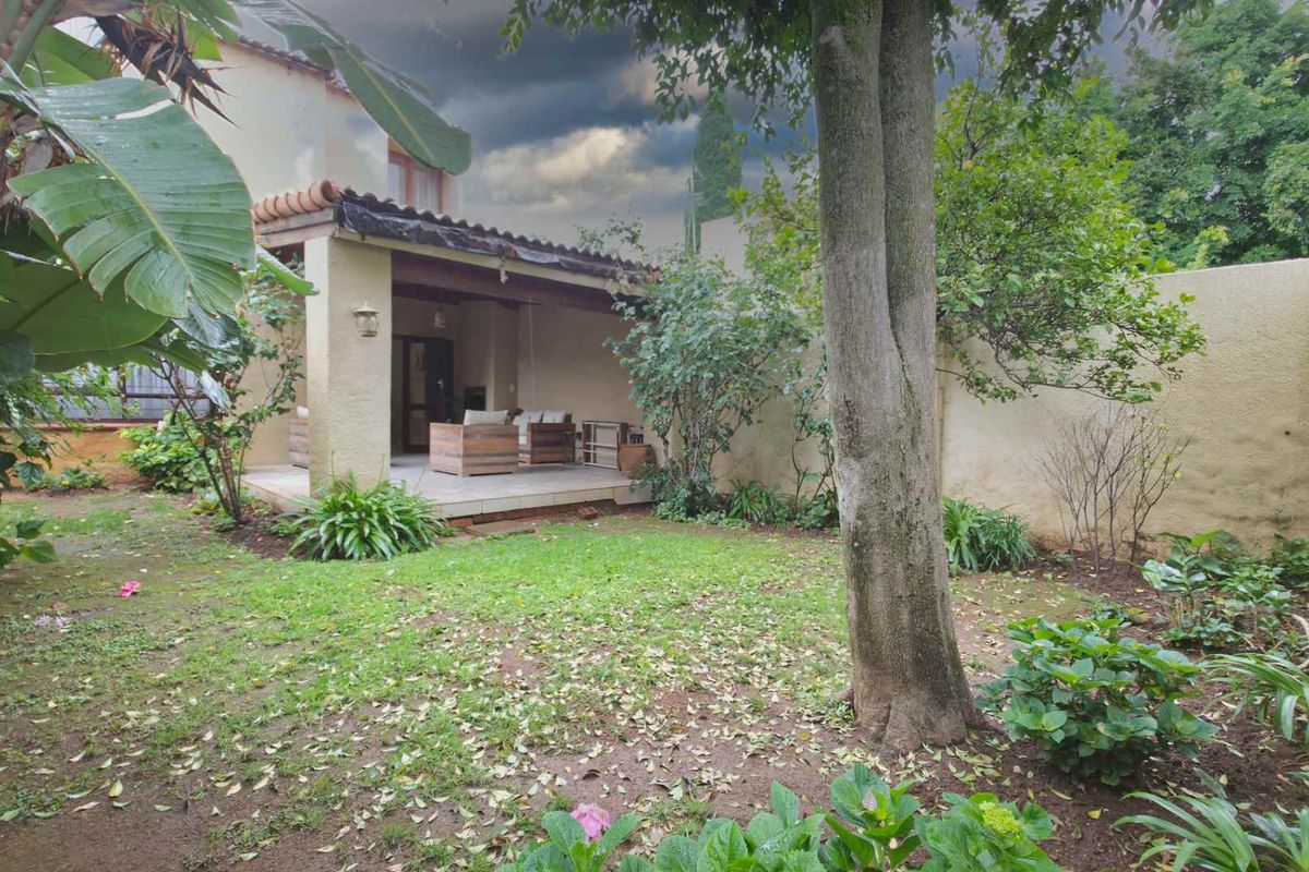A private rear garden featuring a covered patio area, established trees, and perimeter boundary walls, offering a peaceful outdoor space.