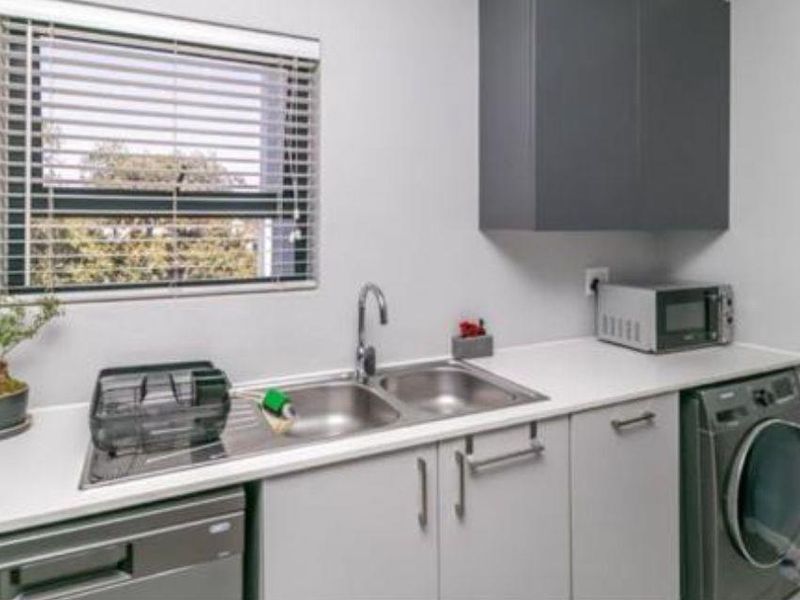 A functional laundry area featuring built-in cabinetry, a double stainless steel sink with mixer tap, and space for under-counter appliances.