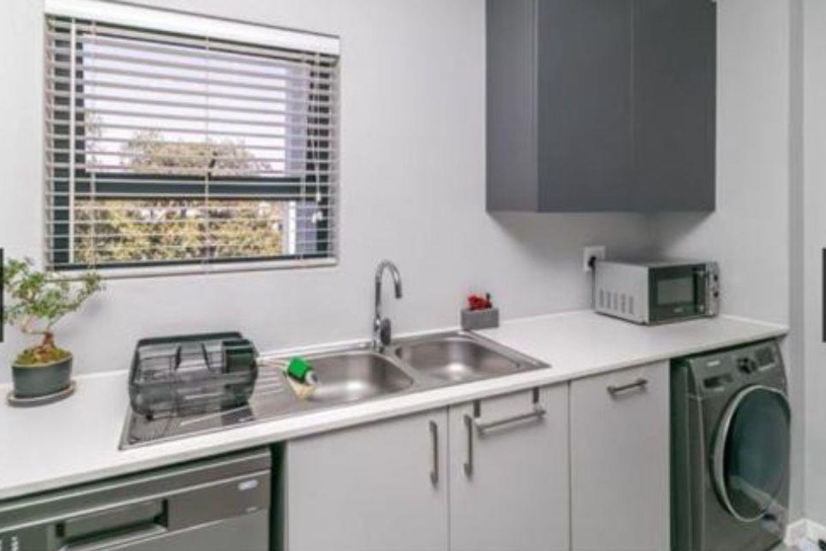 A functional laundry area featuring built-in cabinetry, a double stainless steel sink with mixer tap, and space for under-counter appliances.