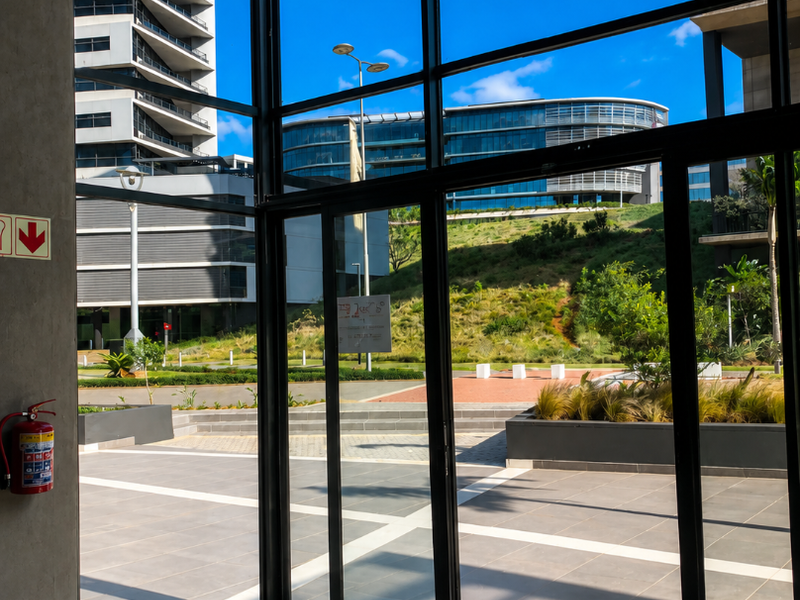 Modern commercial entrance featuring floor-to-ceiling glass panels, sliding doors, and polished tile flooring with views of the surrounding office park.