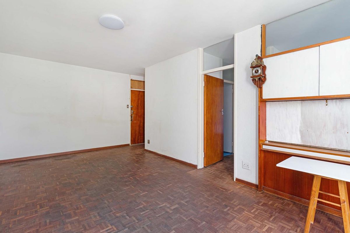 An empty living room featuring original parquet flooring, built-in wooden cabinetry, and neutral wall finishes, offering a blank canvas for renovation.