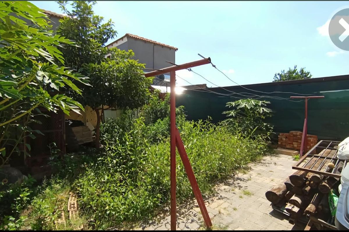 Rear garden area featuring a paved patio, metal washing line, and boundary fencing, currently requiring significant landscaping and maintenance.