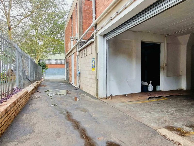Rear industrial exterior featuring a concrete driveway, brick facade, and a large roller shutter door access point.
