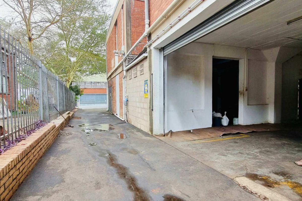 Rear industrial exterior featuring a concrete driveway, brick facade, and a large roller shutter door access point.