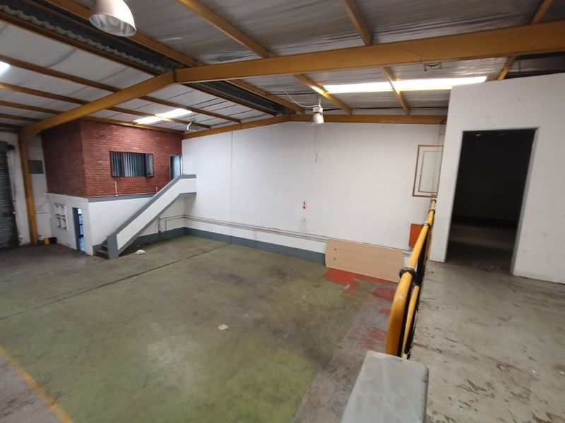 Spacious industrial utility area featuring exposed steel roof trusses, concrete flooring, a mezzanine level with safety railing, and a brickwork feature wall.