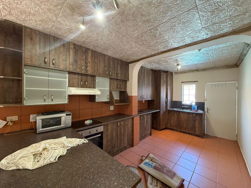 Spacious kitchen featuring wood-look cabinetry, laminate countertops, built-in oven and hob, and tiled flooring with direct access to the exterior.
