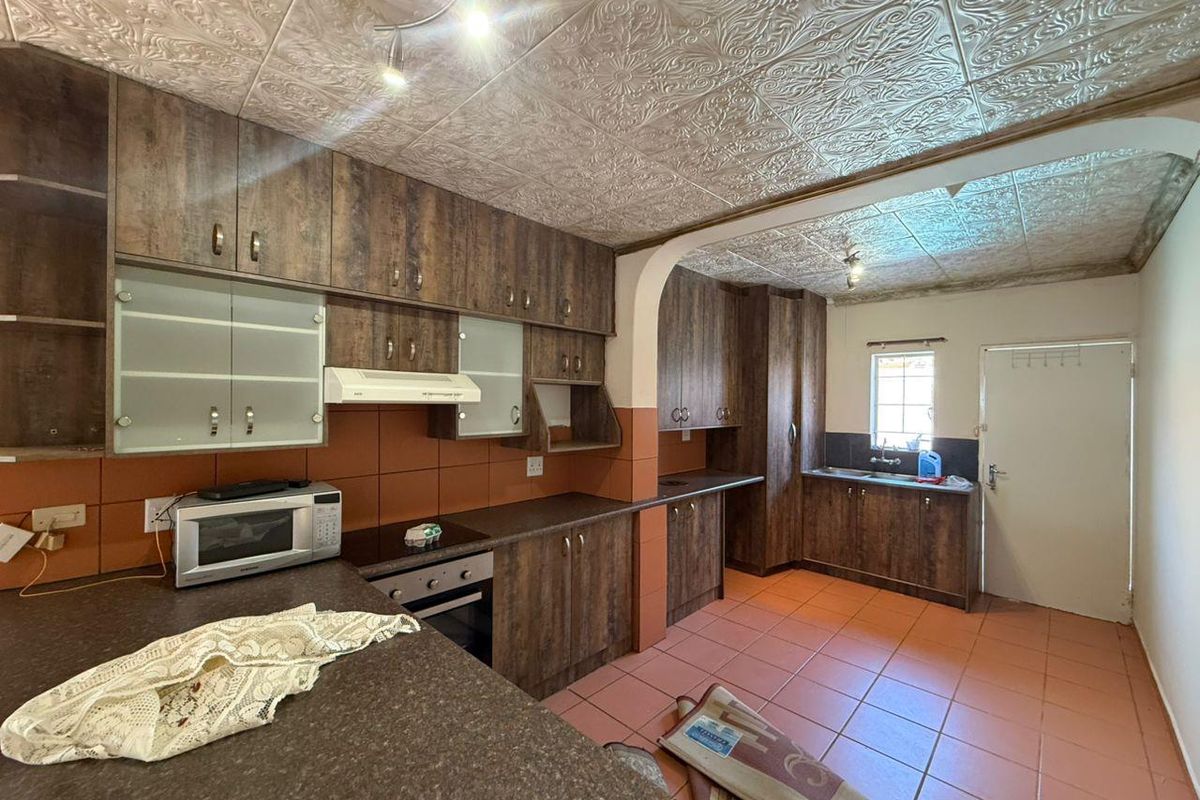 Spacious kitchen featuring wood-look cabinetry, laminate countertops, built-in oven and hob, and tiled flooring with direct access to the exterior.