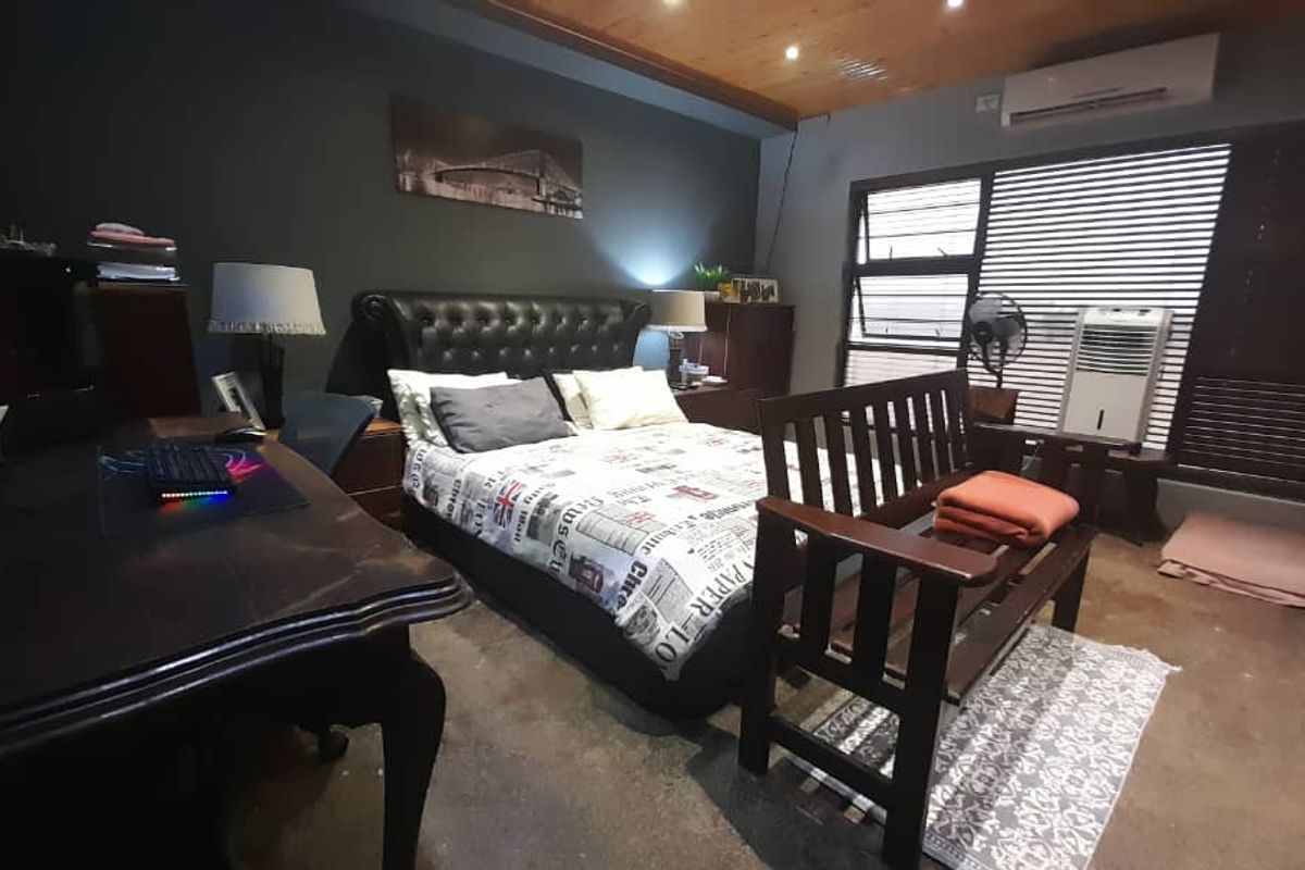 A bedroom featuring a timber-clad ceiling, wall-mounted air conditioning unit, and large windows with horizontal blinds.