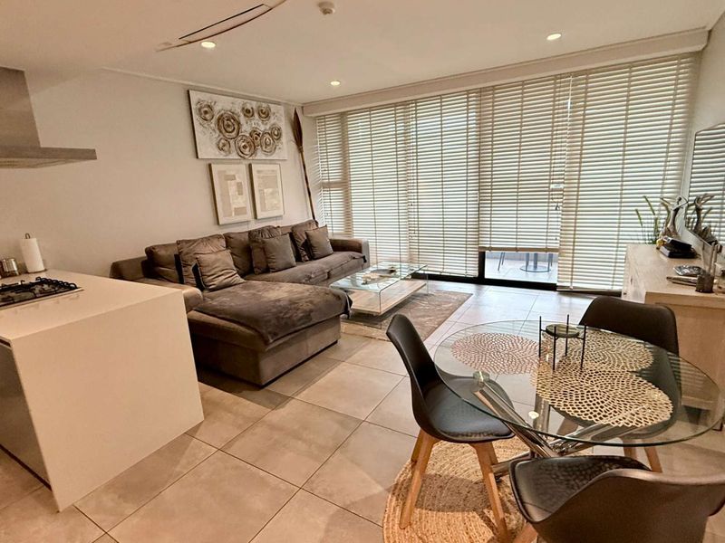 Modern open-plan living area featuring a sleek kitchen island with gas hob, tiled flooring, and large sliding doors leading to an outdoor space.