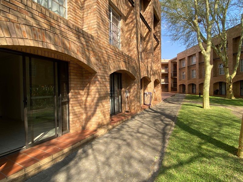 A view of the apartment complex exterior featuring exposed brick architecture, arched detailing, sliding glass access doors, and a well-maintained garden walkway.