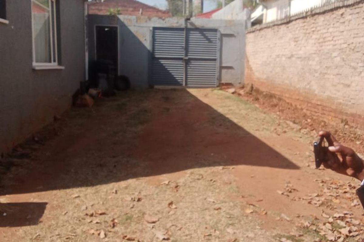 A view of the rear exterior area featuring a dirt yard, boundary wall, and a metal gate providing access to the property.