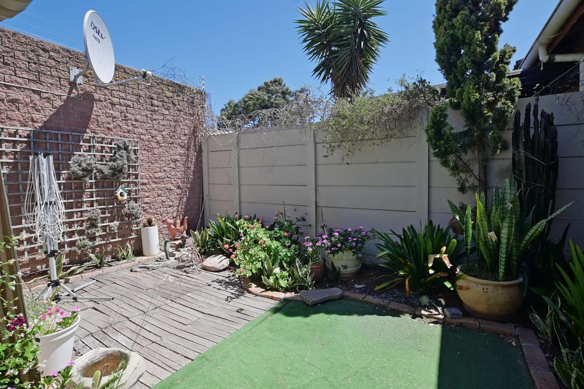 A private rear courtyard featuring a timber deck, artificial lawn area, and perimeter boundary walls with established garden beds.