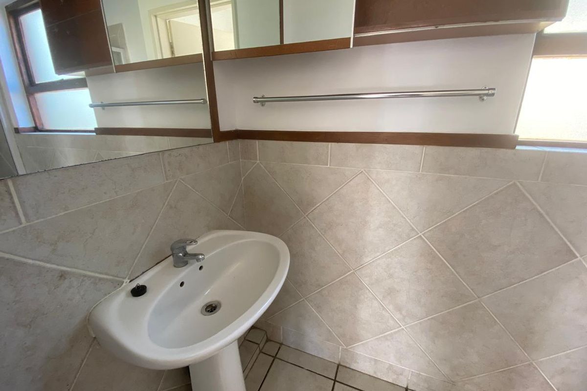 A functional bathroom featuring a pedestal basin, wall-mounted mirror cabinet, and neutral tiled walls.