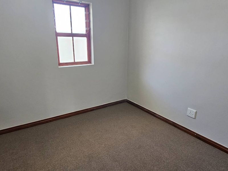 A clean, empty bedroom featuring neutral walls, carpeted flooring, and a window with security bars.