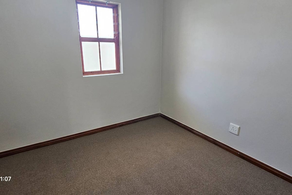 A clean, empty bedroom featuring neutral walls, carpeted flooring, and a window with security bars.