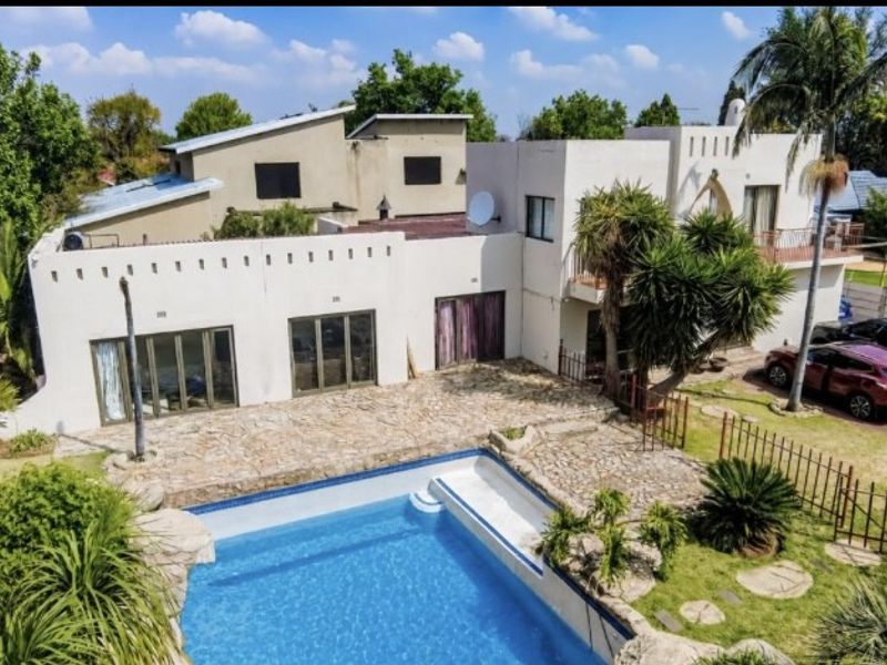 Aerial view of a multi-level residential property featuring a swimming pool, stone-paved patio area, balcony, and driveway.