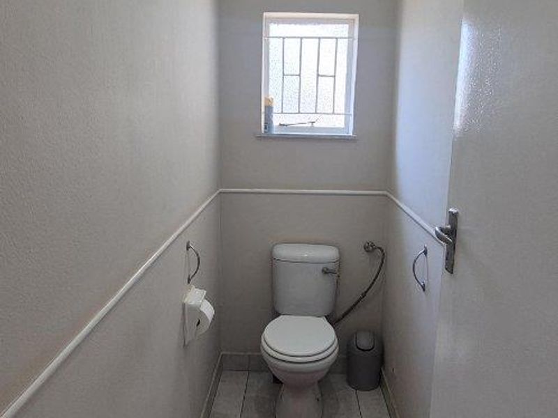 A compact guest toilet featuring tiled flooring, neutral wall finishes, and a security-barred window.