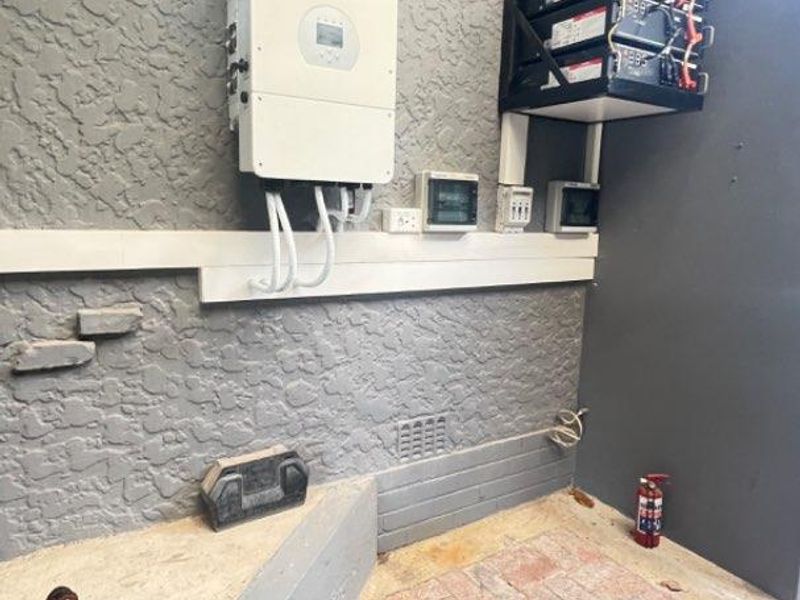 A functional utility area featuring a wall-mounted solar inverter and a stacked lithium battery bank system for off-grid power storage.