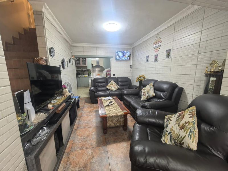 Open plan living area featuring tiled floors and brick-effect wall cladding, with a view through to the kitchen area.