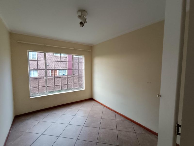A vacant bedroom featuring tiled flooring and a window with security bars, offering a blank canvas for personalization.