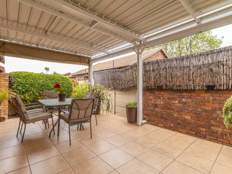 A covered outdoor patio featuring tiled flooring, a corrugated metal roof, and a brick boundary wall with a privacy screen.