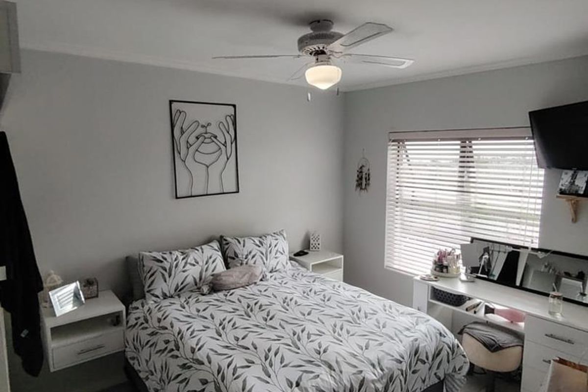 A well-maintained bedroom featuring tiled flooring, a central ceiling fan, and venetian blinds, providing a clean and functional living space.