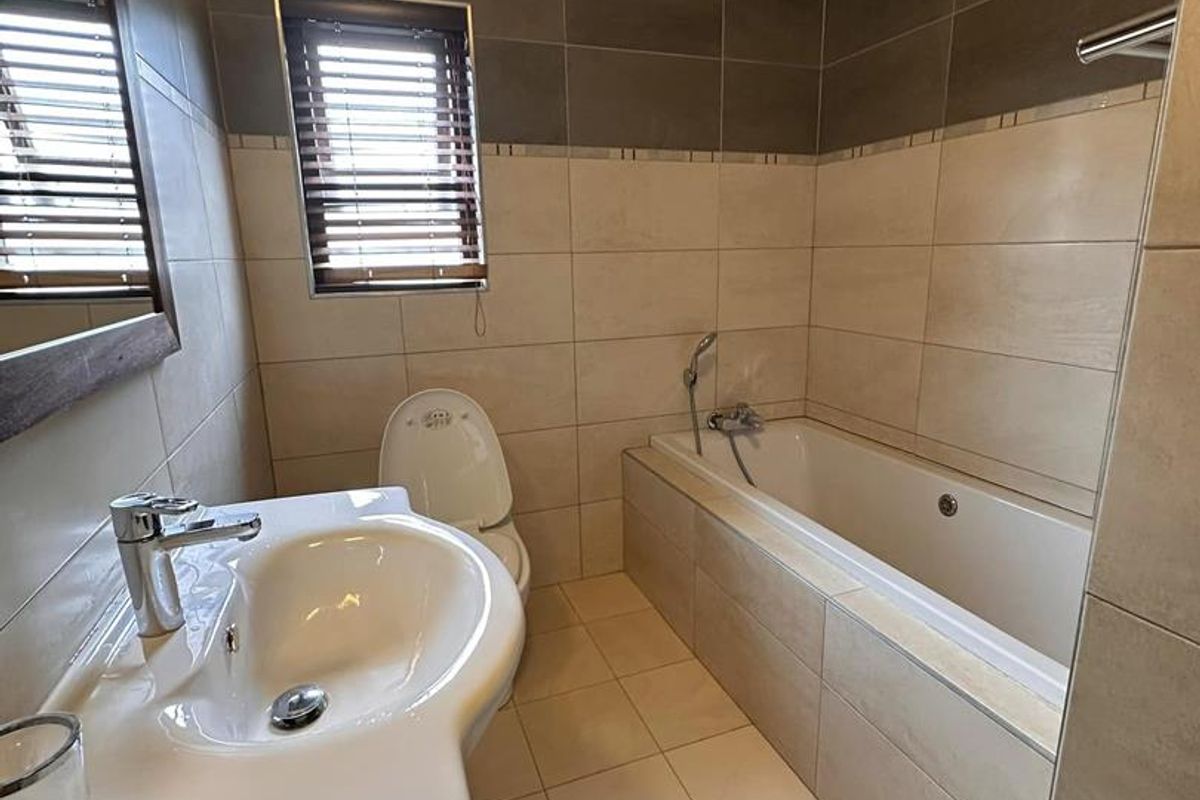 A well-maintained bathroom featuring a built-in bathtub, a modern vanity basin, and neutral-toned wall and floor tiling.