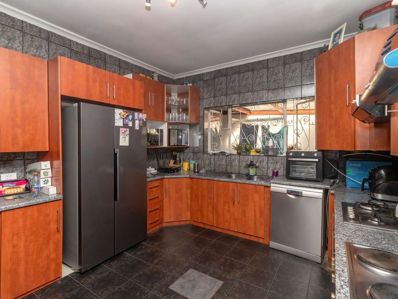 A functional kitchen featuring wood-look cabinetry, granite countertops, a gas hob, and tiled finishes throughout, offering a practical layout for daily meal preparation.