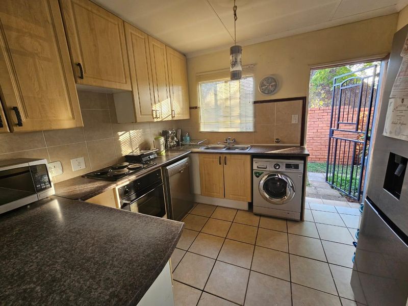 Functional kitchen featuring laminate cabinetry, built-in oven, electric hob, and tiled flooring with direct access to the rear exterior area.