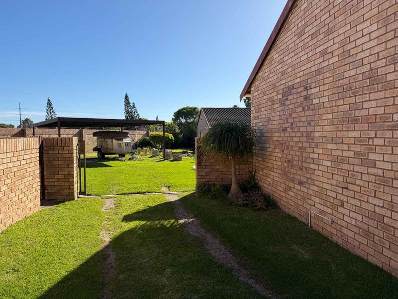 A view of the rear garden area featuring a brick boundary wall, a lawn, and a metal carport structure.