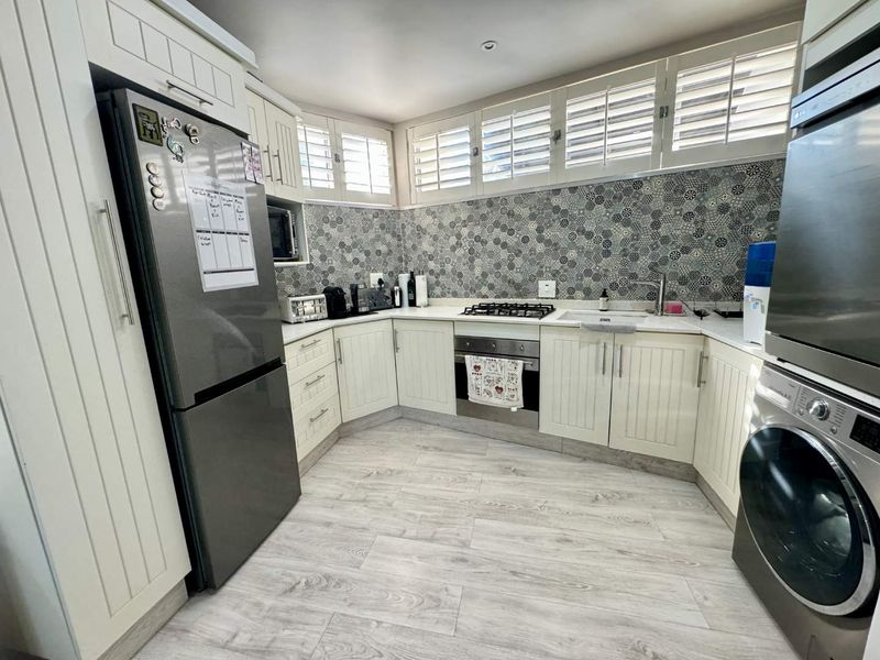 Modern kitchen featuring white cabinetry, patterned tiled backsplash, gas hob, built-in oven, and plantation shutters, offering a clean and functional workspace.