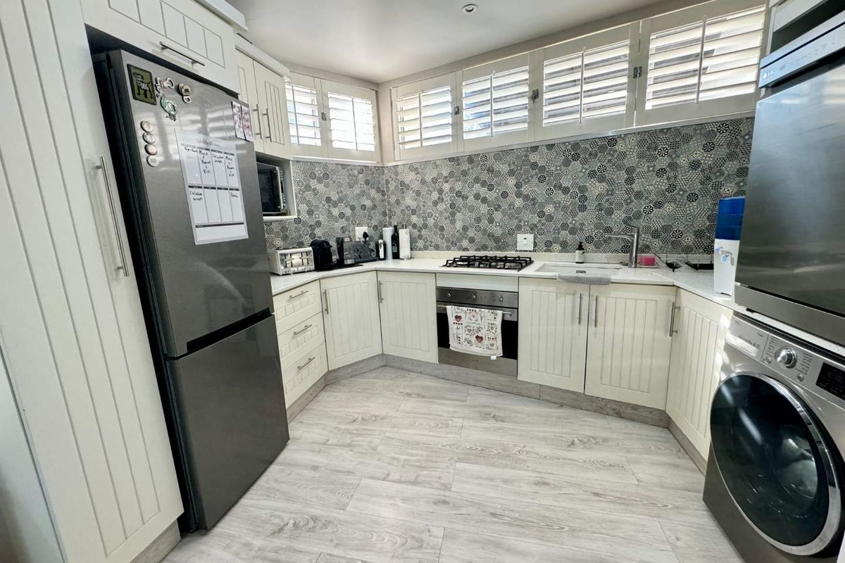 Modern kitchen featuring white cabinetry, patterned tiled backsplash, gas hob, built-in oven, and plantation shutters, offering a clean and functional workspace.